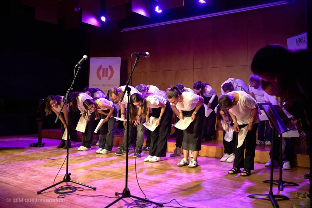Els cantaires, amb les partitures a les mans, fan una reverència damunt l'escenari il·luminat de lila, entre micròfons i faristols.