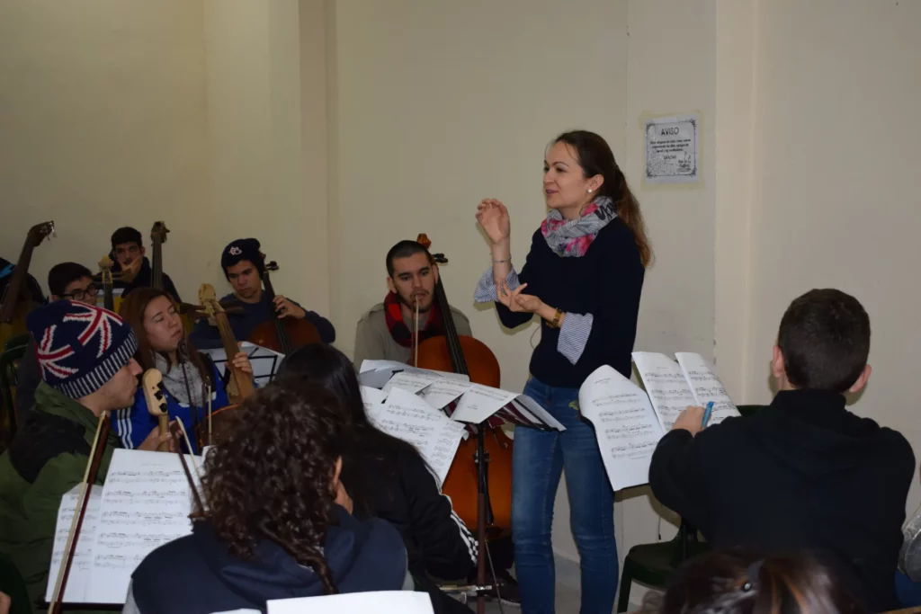 Lana Kovačević dempeus dirigint-se als joves músics de l'orquestra durant un assaig, envoltada d'atrils i violoncels.