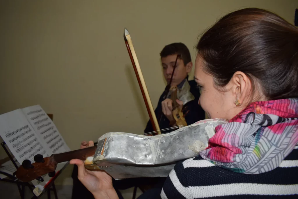 Primer pla d'un violí amb la caixa feta de xapa d'alumini, tocat per una noia davant d'una partitura.