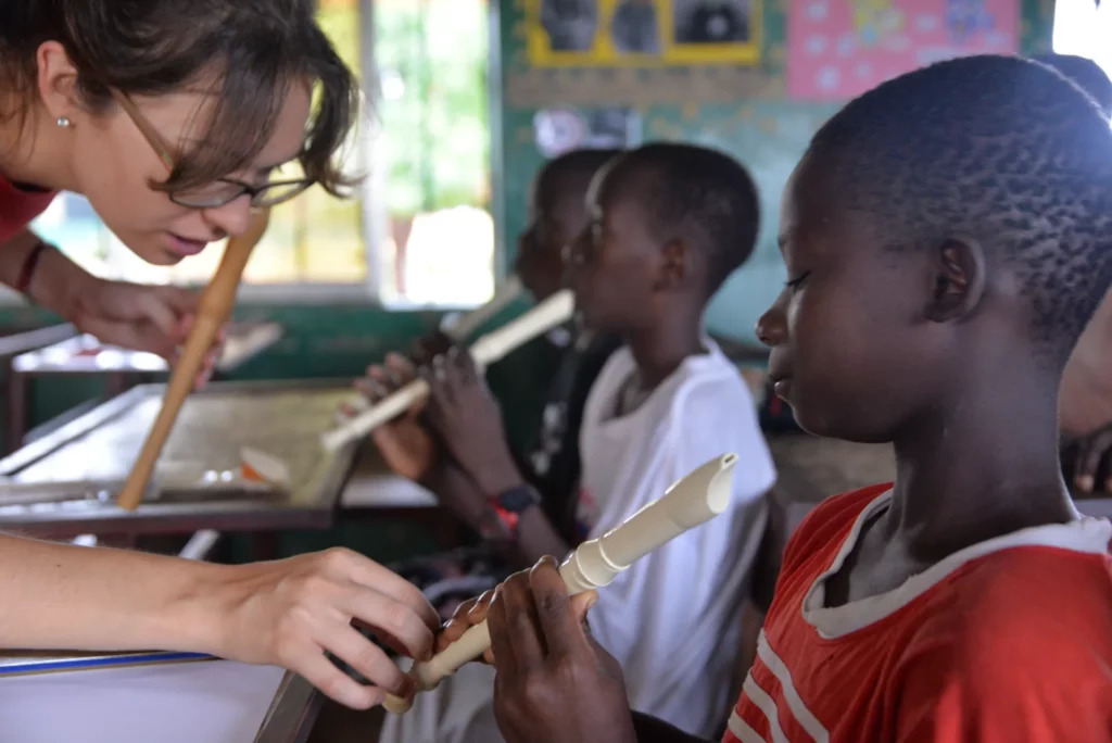 Lana Kovačević s'inclina per ajudar un nen a col·locar els dits a la flauta dolça, mentre altres infants de la classe proven la seva.
