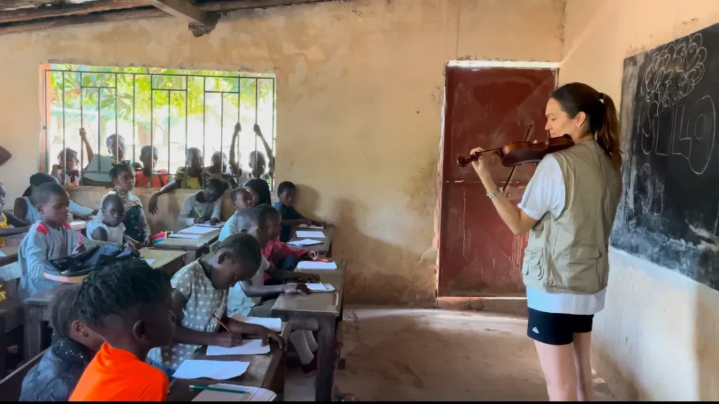 Lana Kovačević toca el violí davant d'una aula d'infants que l'escolten des dels pupitres, amb altres nens mirant per la finestra.